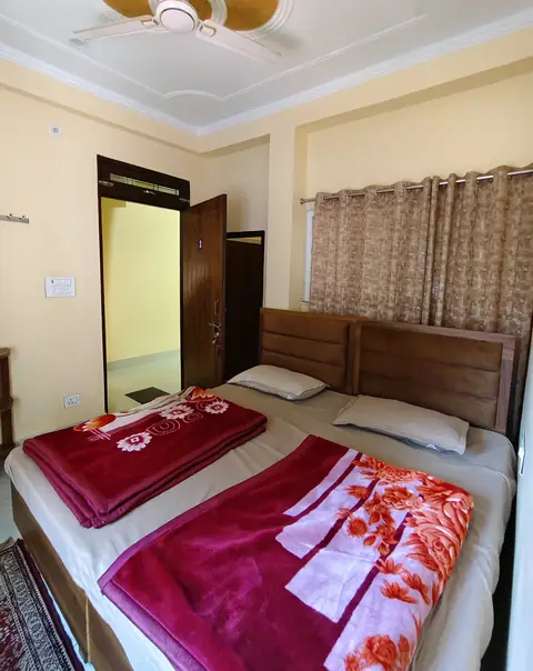 A double room with red blankets and the door open to the corridor