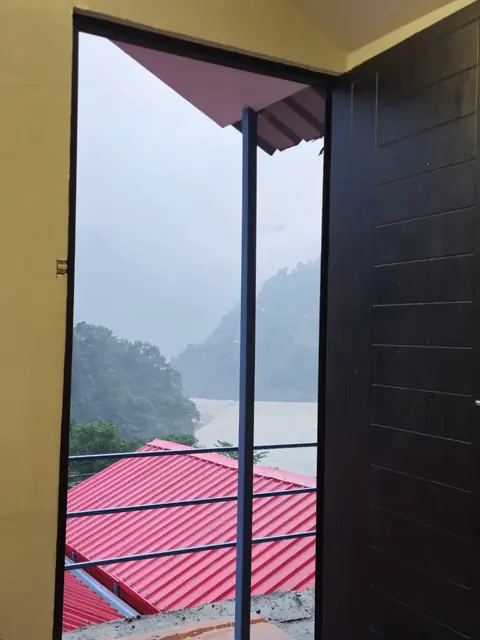 The view from a cottage door over red roofs to the Ganga and misty hills