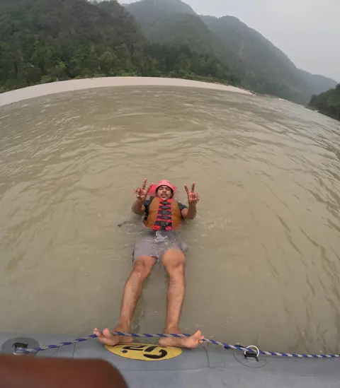 A rafter floats on his back in the Ganga in a helmet and life jacket, feet hooked on the raft’s rope