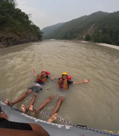 Two rafters float side by side in the Ganga between forested hills