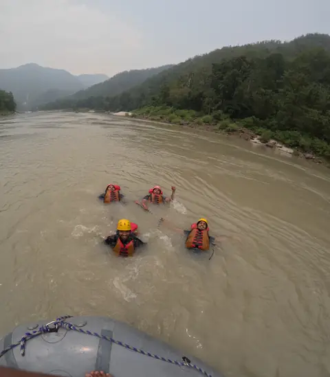 Four rafters in helmets and life jackets float in the Ganga beside the raft