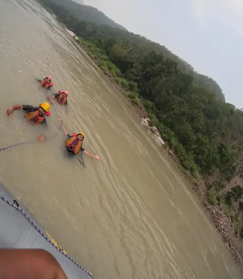 Four rafters swim beside the raft, holding its safety rope