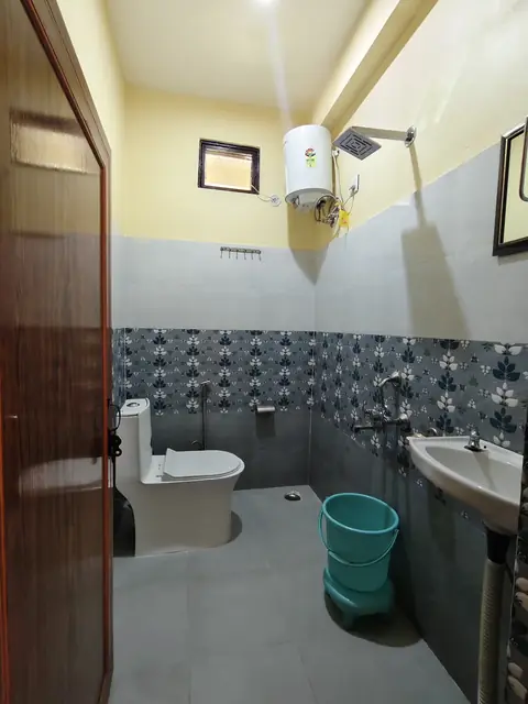 A bathroom with a western toilet, a wash basin, a shower and a geyser