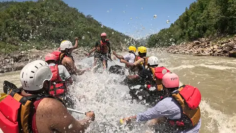 A wave splashes over the raft and its crew in a rapid