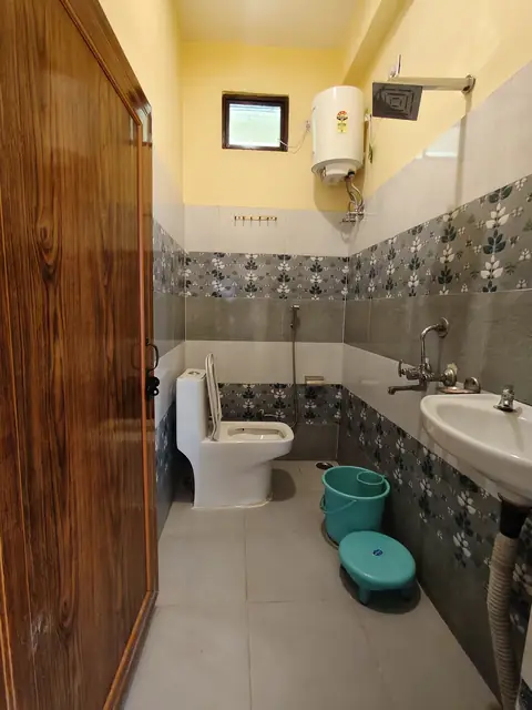 A bathroom with grey tiles, a shower, a geyser and a wash basin