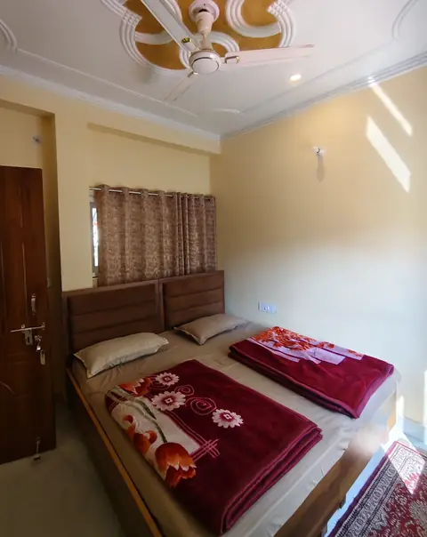 A double room with red blankets and a curtained window behind the bed